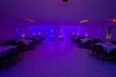 Parking extérieur de nuit avec une voiture stationnée, éclairé par des lampadaires et entouré de haies et d'arbres.