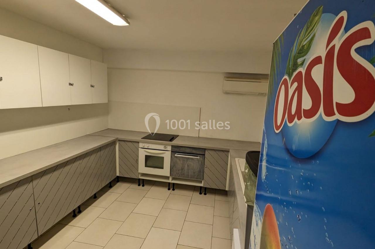 Cuisine équipée avec placards blancs, plan de travail gris, four, lave-vaisselle et affiche publicitaire Oasis au premier…