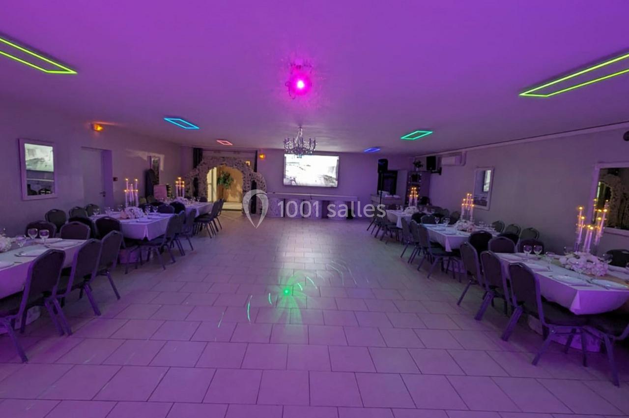 Salle de réception décorée avec des tables dressées, éclairage coloré et grand écran au fond.