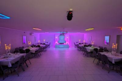 Parking extérieur de nuit avec une voiture stationnée, éclairé par des lampadaires et entouré de haies et d'arbres.