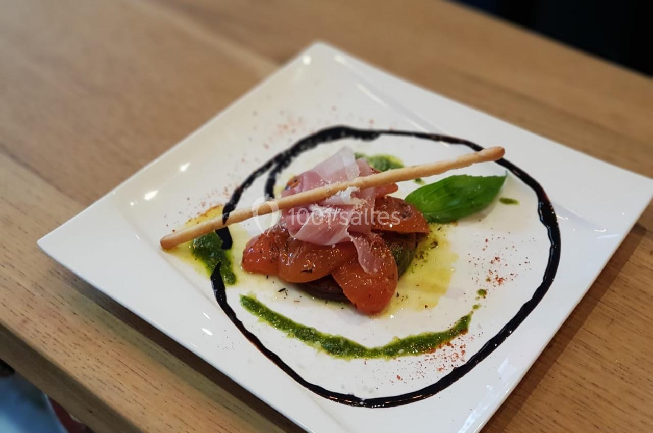 Assiette de tomates confites avec jambon cru, pesto, réduction balsamique et un gressin, servie sur une table en bois.