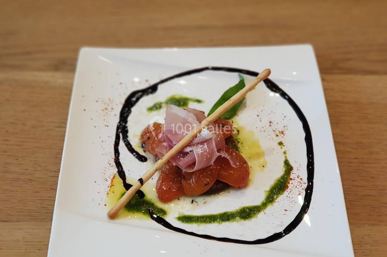 Assiette de carpaccio de tomates avec jambon cru, grissini, et sauces décoratives sur une table en bois.