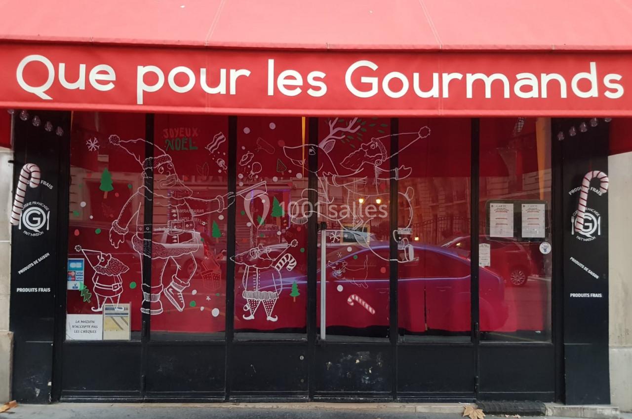 Façade d'une boutique avec une vitrine décorée sur le thème de Noël et une enseigne rouge indiquant ’Que pour les Gourmands’.