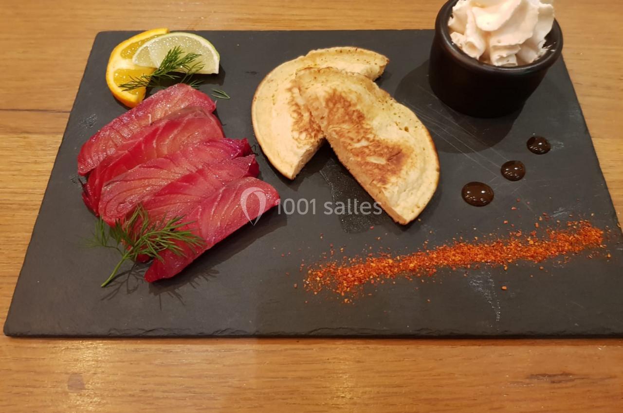 Assiette de saumon fumé avec blinis, crème fouettée, tranche de citron et épices sur une ardoise noire.