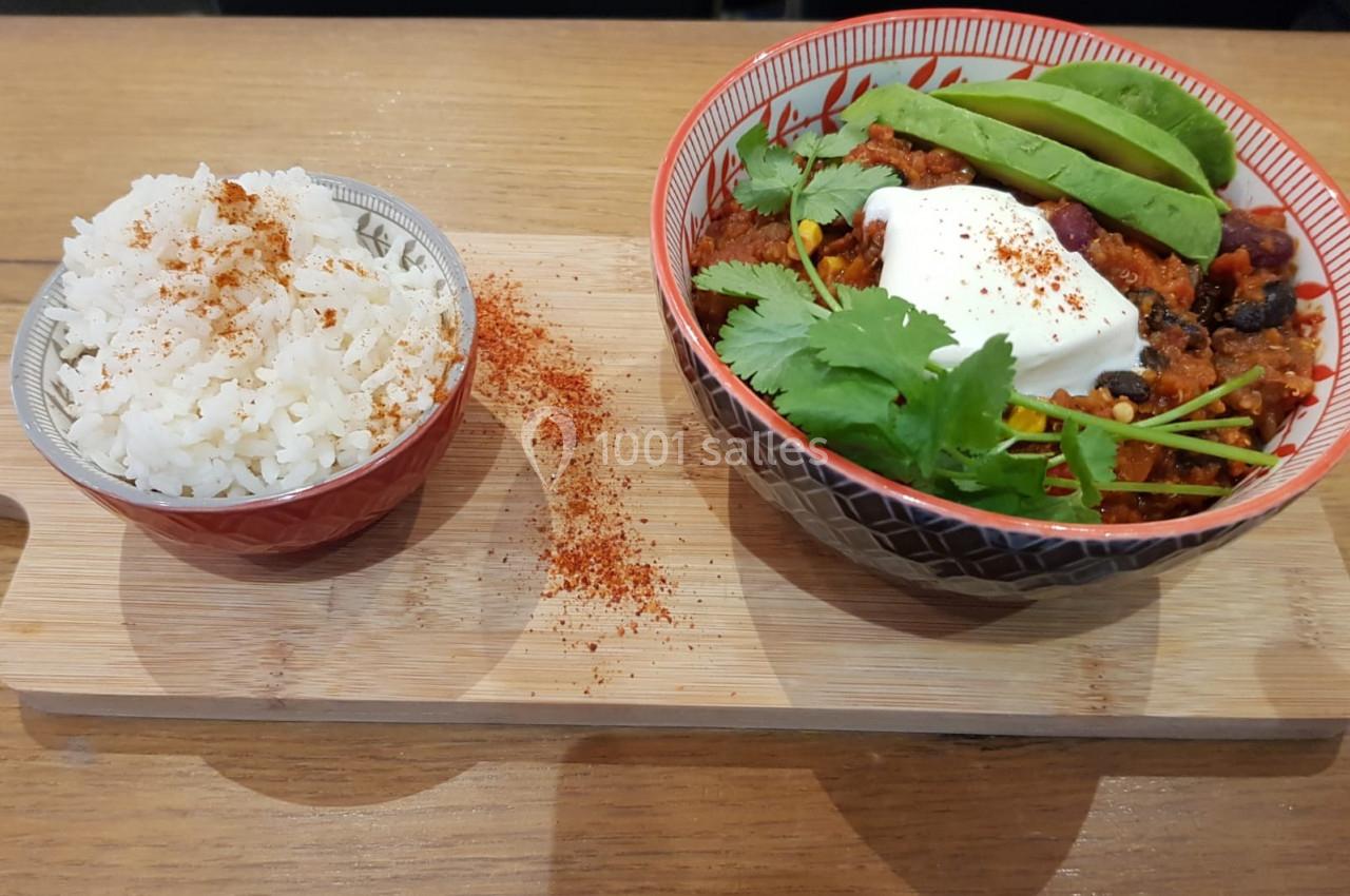 Bol de chili garni d'avocat, crème et coriandre, accompagné de riz blanc saupoudré de paprika sur une planche en bois.