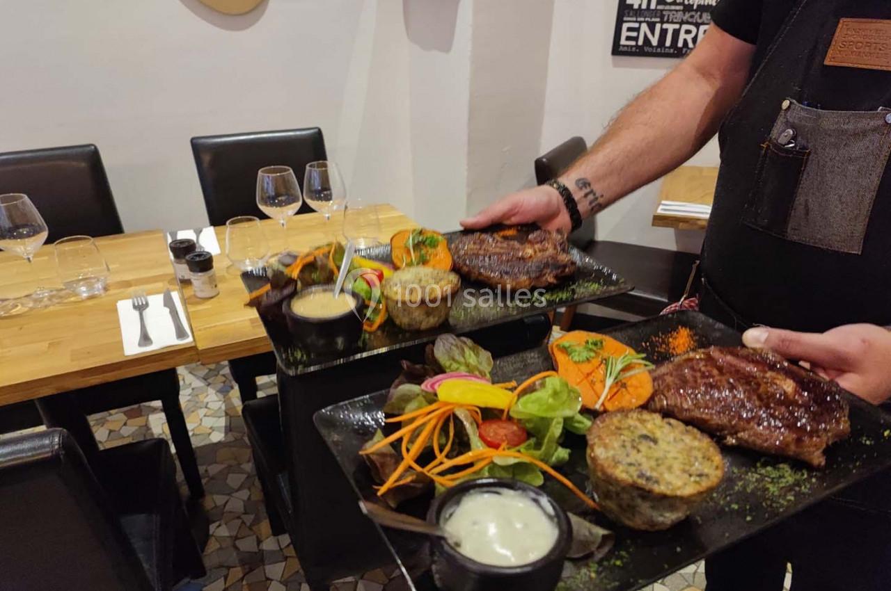Un serveur apporte deux assiettes garnies de steaks, légumes, sauces et accompagnements dans un restaurant.