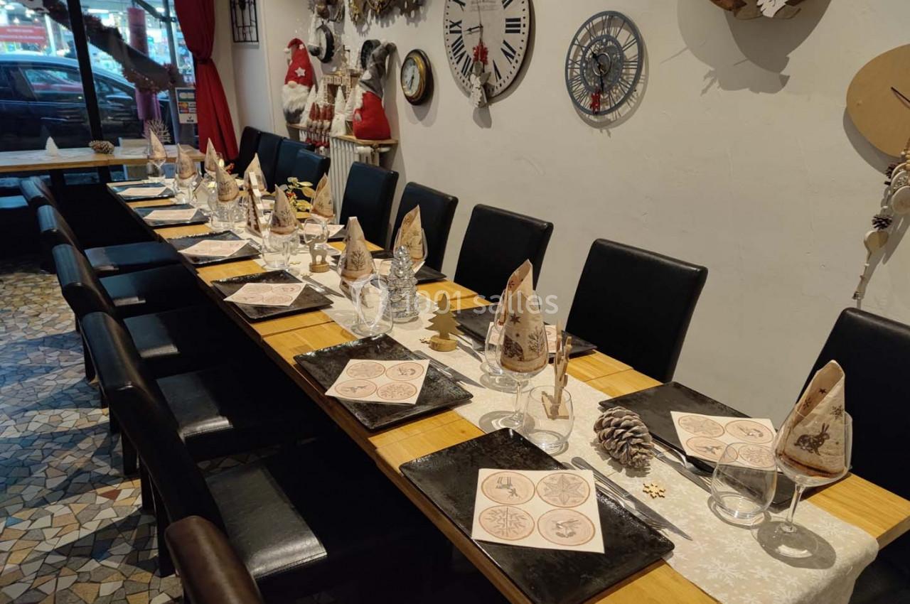 Table décorée pour un repas, avec serviettes pliées, assiettes noires, verres et décorations de Noël sur un chemin de table.