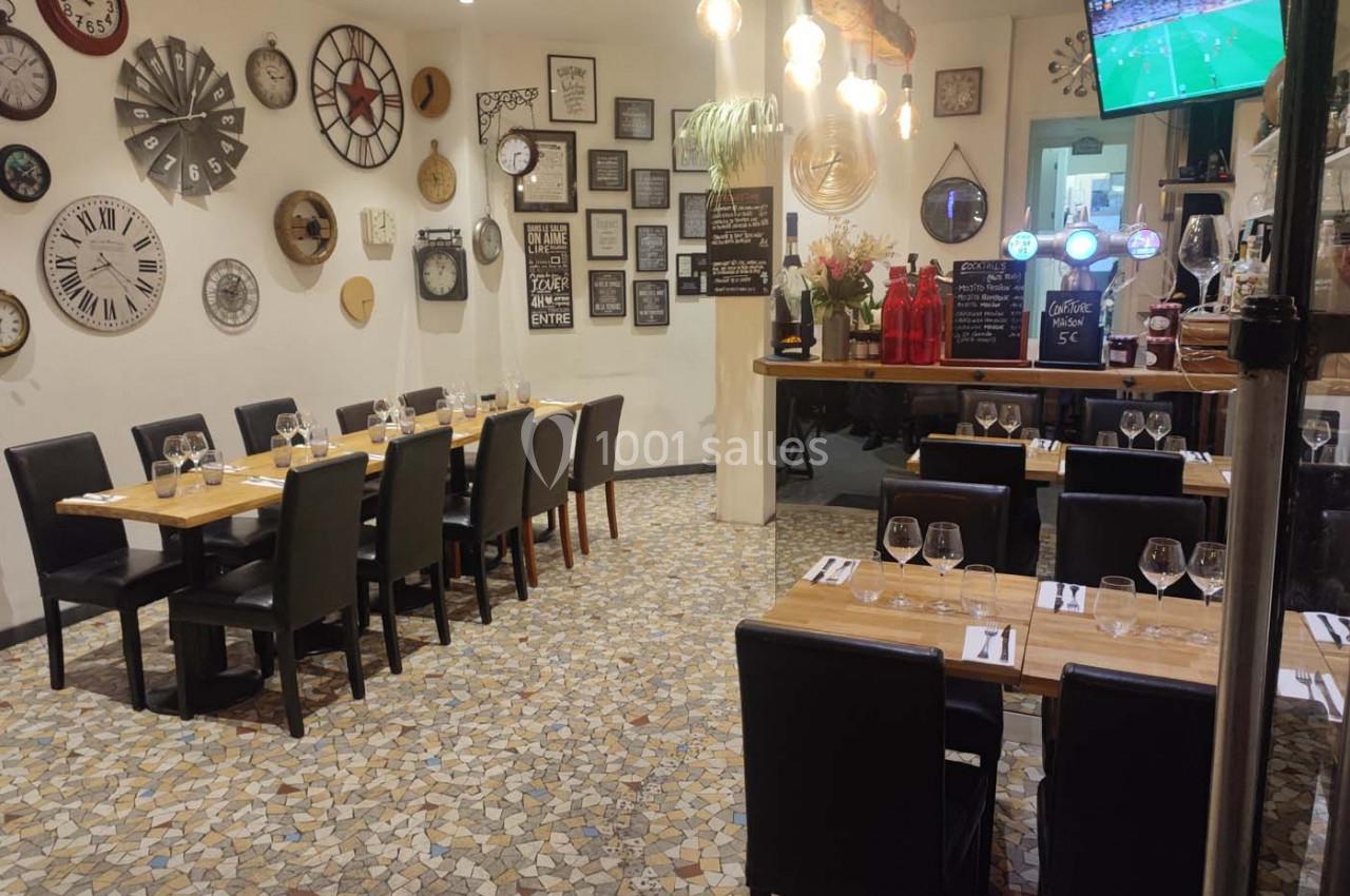 Salle de restaurant décorée de nombreuses horloges murales, avec tables dressées et écran diffusant un match.