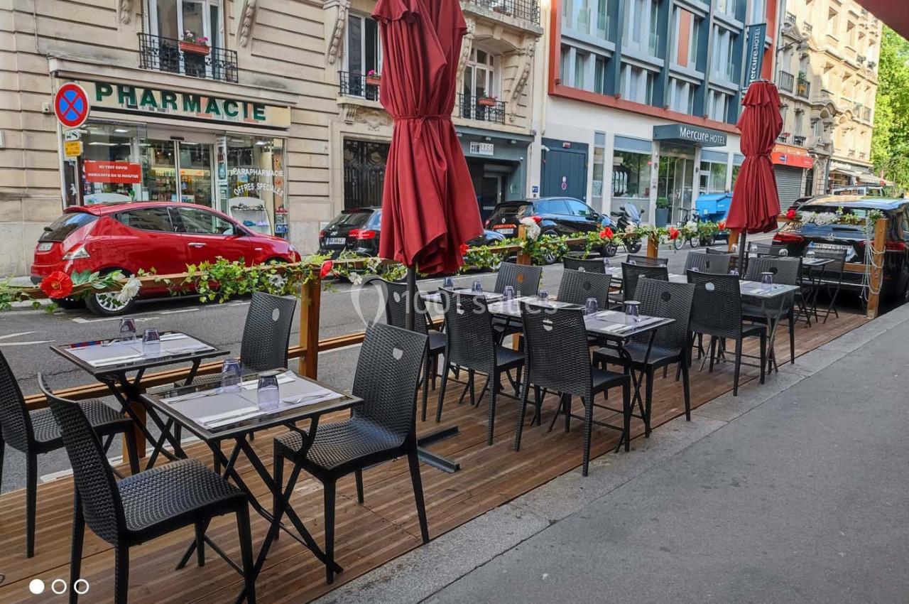 Terrasse de restaurant avec tables et chaises noires alignées, située sur un trottoir en bordure de rue urbaine.