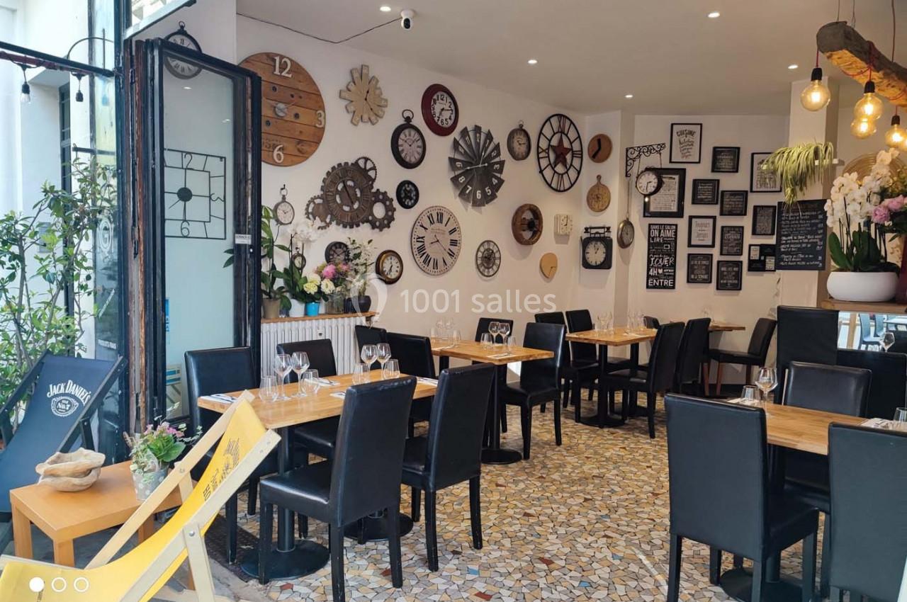 Salle de restaurant décorée avec des horloges murales, des tables en bois et des chaises noires sur un sol en mosaïque.