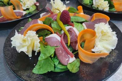 Assiette de salade composée avec magret de canard, carottes, fromage, framboise et feuilles de salade verte.