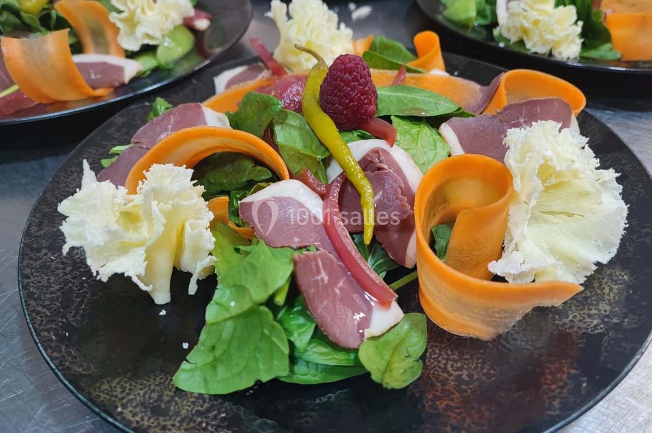 Assiette de salade composée avec magret de canard, carottes, fromage, framboise et feuilles de salade verte.