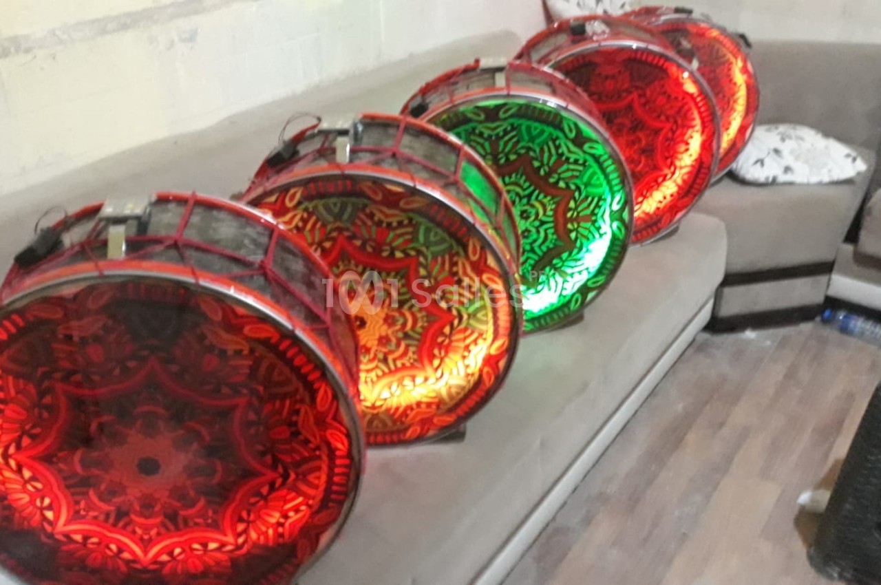 Tambours décoratifs éclairés de motifs rouges et verts, alignés sur un canapé dans une pièce au sol en bois.