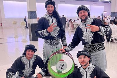 Un couple en tenue traditionnelle pose entouré de musiciens en costume jouant du tambour dans une salle décorée.
