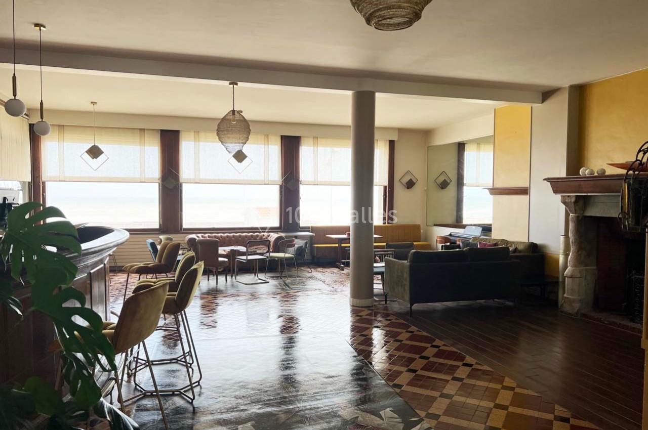 Intérieur lumineux d'un salon avec bar, fauteuils, grandes fenêtres et sol en mosaïque colorée.