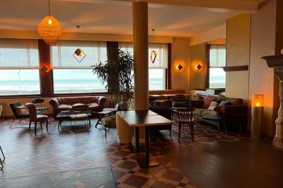 Terrasse en bord de mer avec chaises, tables, espace gazonné et un kiosque blanc sous un ciel partiellement nuageux.