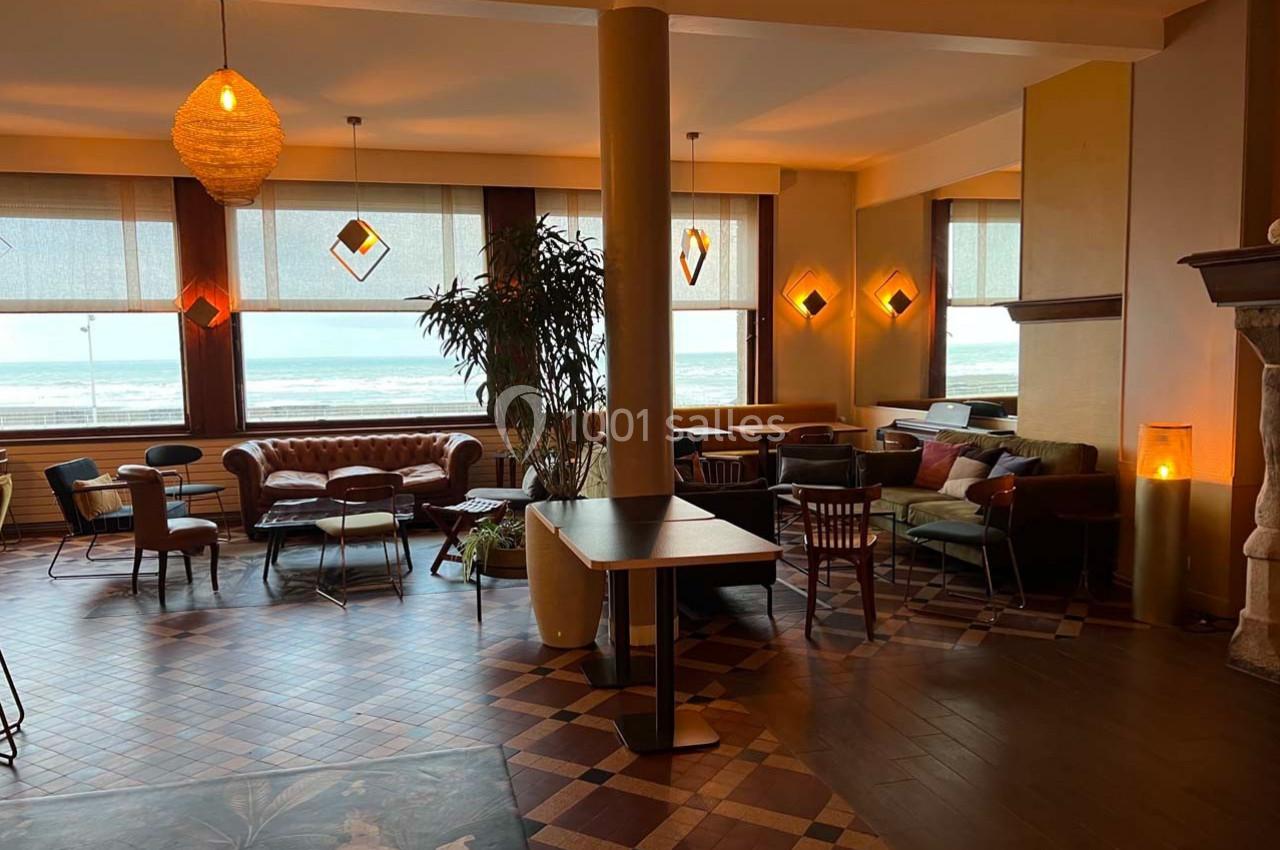 Salle lumineuse avec vue sur la mer, décorée de meubles variés, plantes et luminaires suspendus.