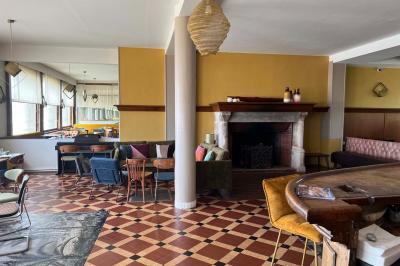 Terrasse en bord de mer avec chaises, tables, espace gazonné et un kiosque blanc sous un ciel partiellement nuageux.
