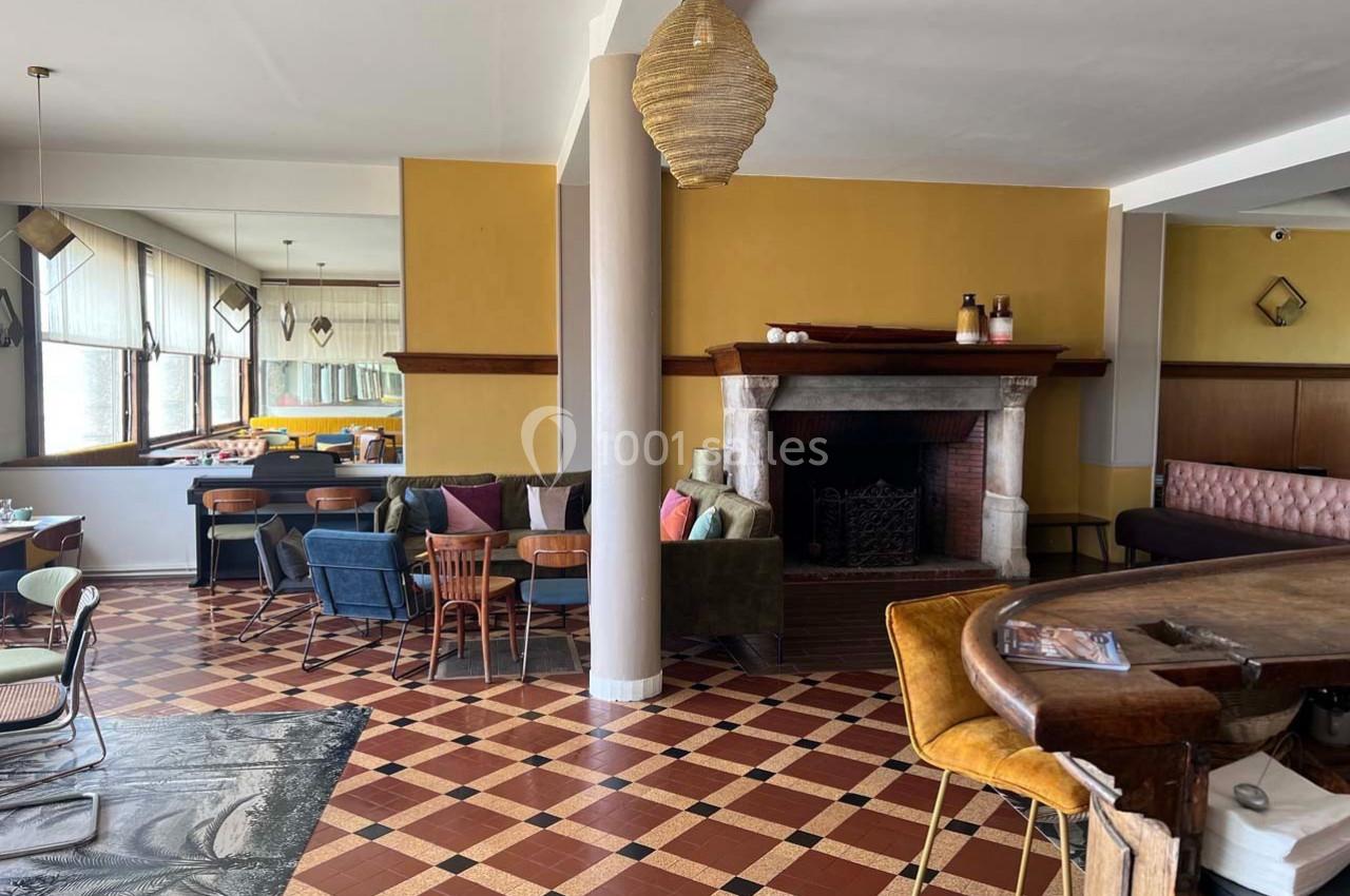 Salle lumineuse avec cheminée, mobilier varié et carrelage en damier rouge et beige, ambiance chaleureuse.