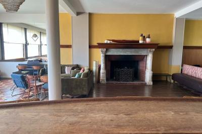 Terrasse en bord de mer avec chaises, tables, espace gazonné et un kiosque blanc sous un ciel partiellement nuageux.