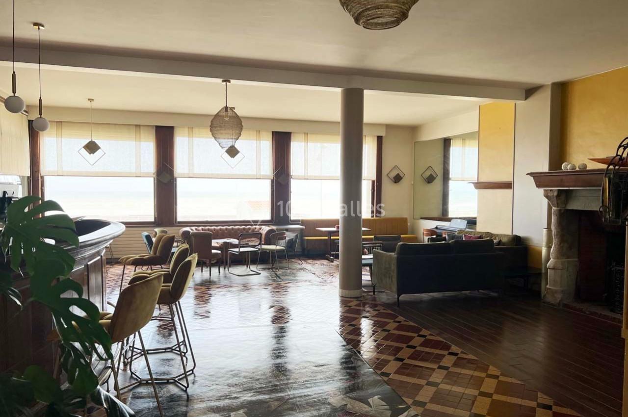 Intérieur d'un salon lumineux avec des fauteuils, un bar, des fenêtres donnant sur l'extérieur et un sol en mosaïque.