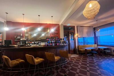Terrasse en bord de mer avec chaises, tables, espace gazonné et un kiosque blanc sous un ciel partiellement nuageux.