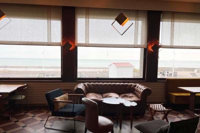 Terrasse en bord de mer avec chaises, tables, espace gazonné et un kiosque blanc sous un ciel partiellement nuageux.