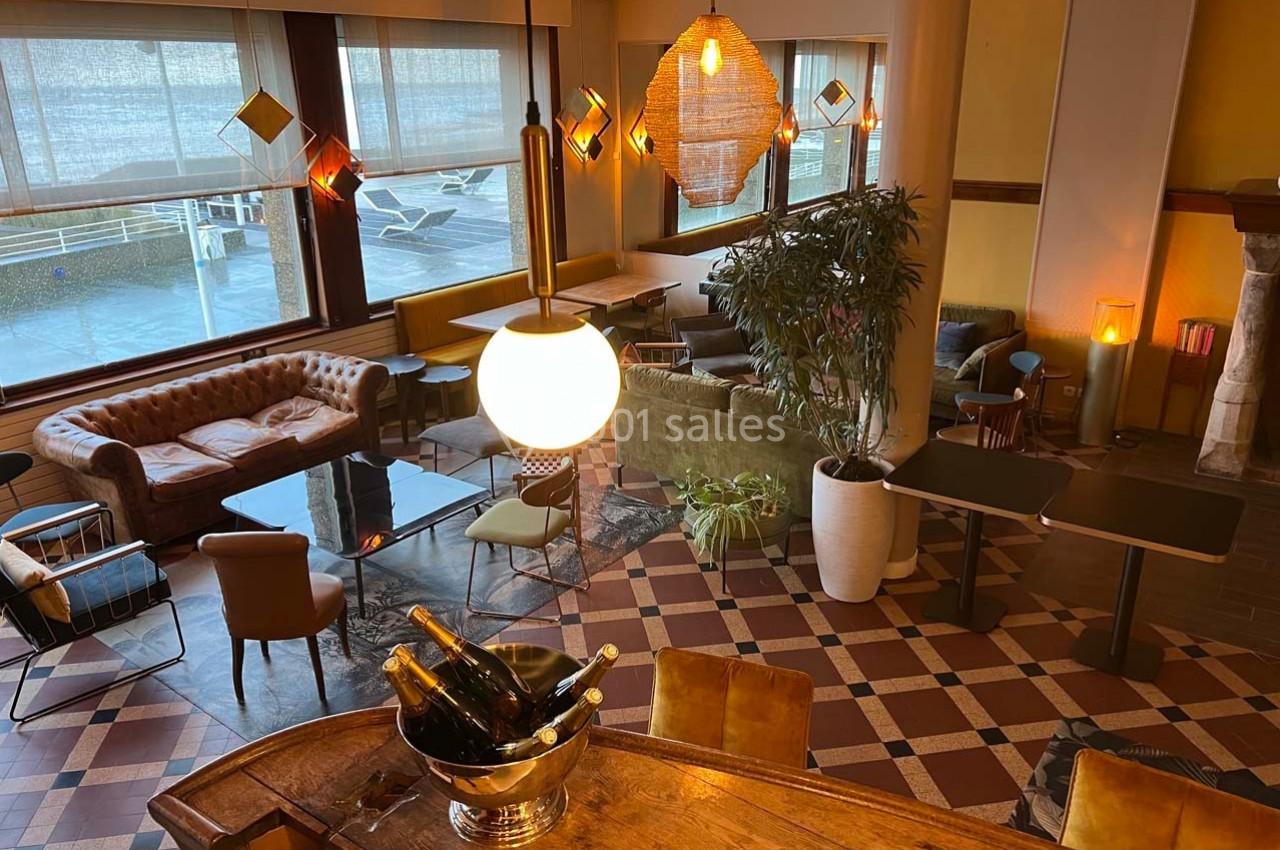 Espace intérieur lumineux avec mobilier éclectique, canapés, tables, plantes et un bar avec des bouteilles de champagne.