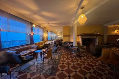 Terrasse en bord de mer avec chaises, tables, espace gazonné et un kiosque blanc sous un ciel partiellement nuageux.