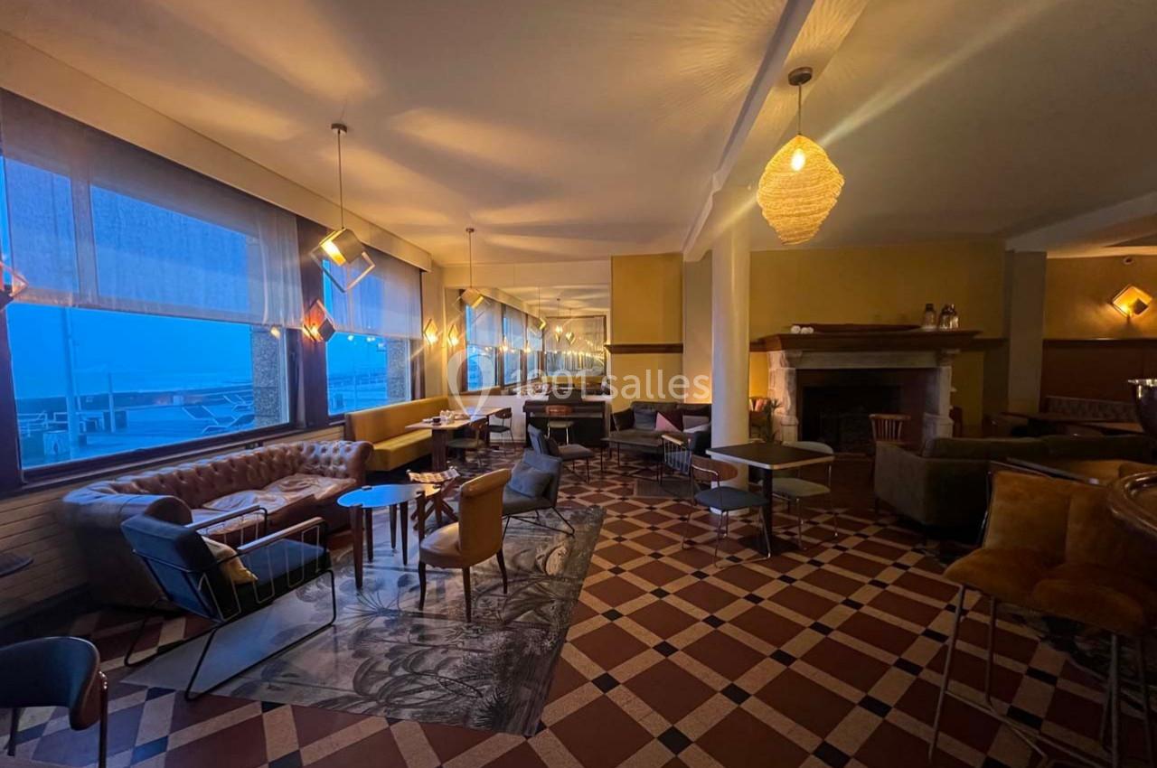 Salle de restaurant chaleureuse avec mobilier varié, éclairage tamisé et grandes fenêtres donnant sur l'extérieur.