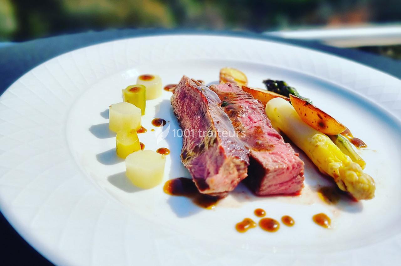 Assiette gastronomique avec viande grillée, asperges, pommes de terre et sauce, présentée sur une table élégante.