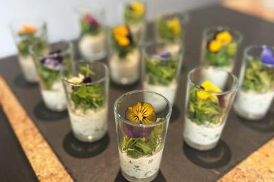 Verrines garnies de crème aux herbes, salade verte et fleurs comestibles, présentées sur un plateau noir.