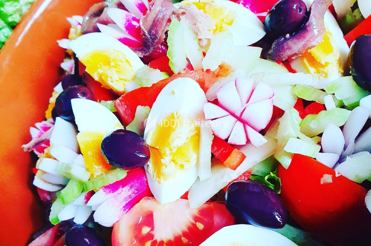 Salade composée avec œufs durs, tomates, radis, olives noires, anchois et légumes variés dans un plat en terre cuite.