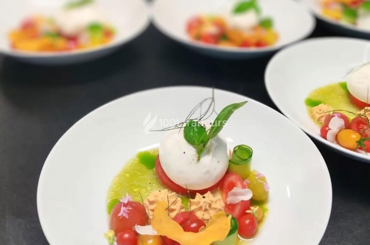 Assiette de burrata accompagnée de légumes colorés, herbes fraîches et sauce verte, présentée sur une table noire.