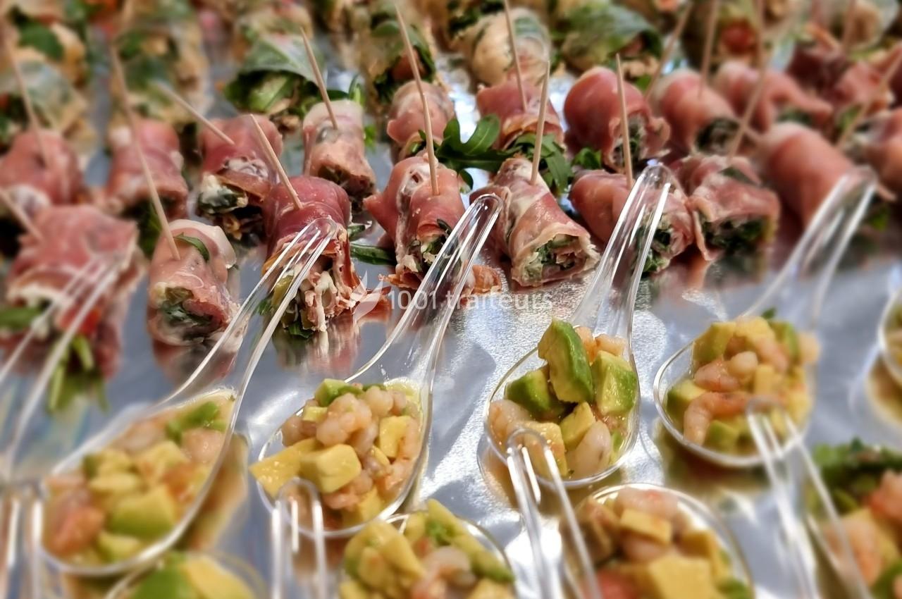 Bouchées apéritives composées de roulés de jambon cru et de cuillères garnies de crevettes, avocat et légumes.