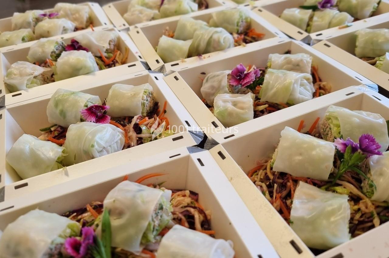 Plateaux de rouleaux de printemps garnis de légumes colorés et décorés de fleurs comestibles.