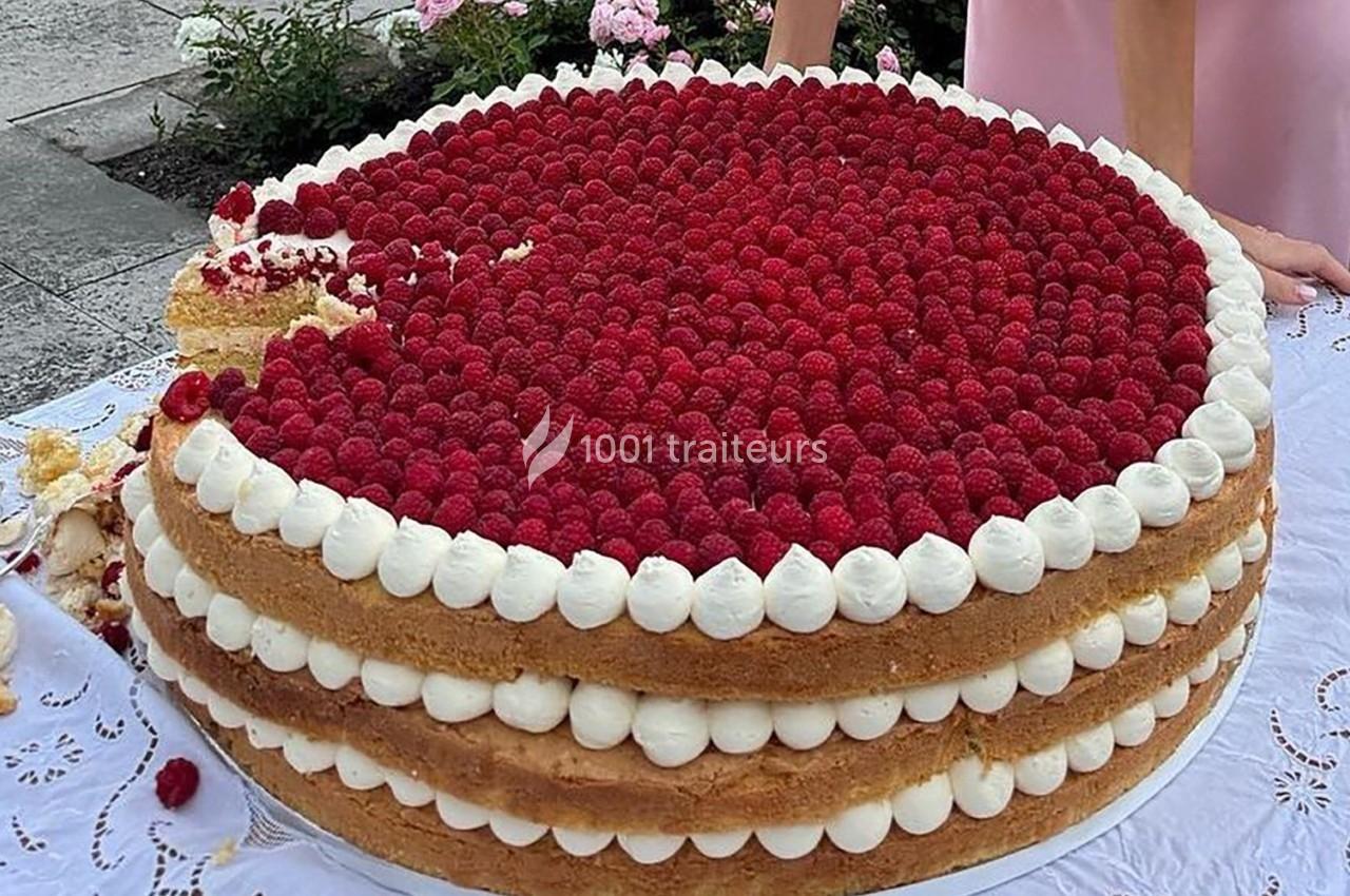 Gâteau à étages garni de framboises et de crème, présenté sur une nappe blanche en extérieur.