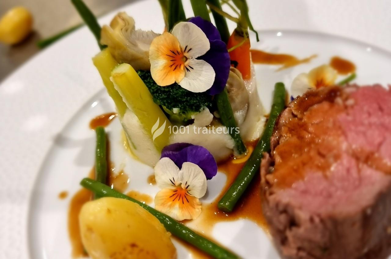 Assiette gastronomique avec viande rosée, légumes variés, purée, fleurs comestibles et sauce.