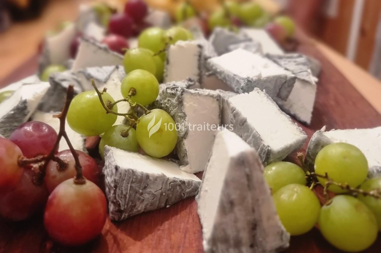 Assortiment de morceaux de fromage à croûte cendrée entourés de raisins verts et rouges sur une planche en bois.