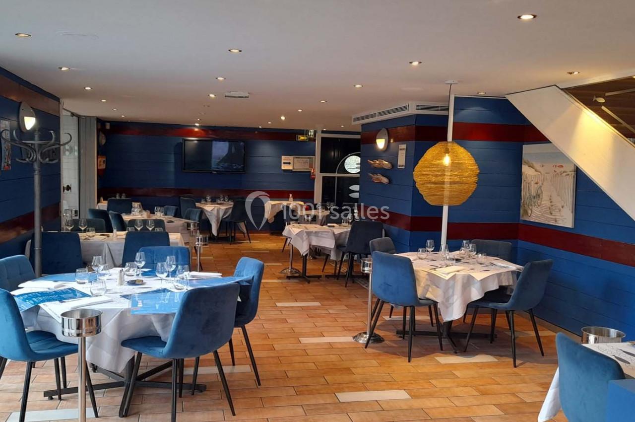 Salle de restaurant lumineuse avec tables dressées, chaises bleues, murs en bois bleu et décoration maritime.
