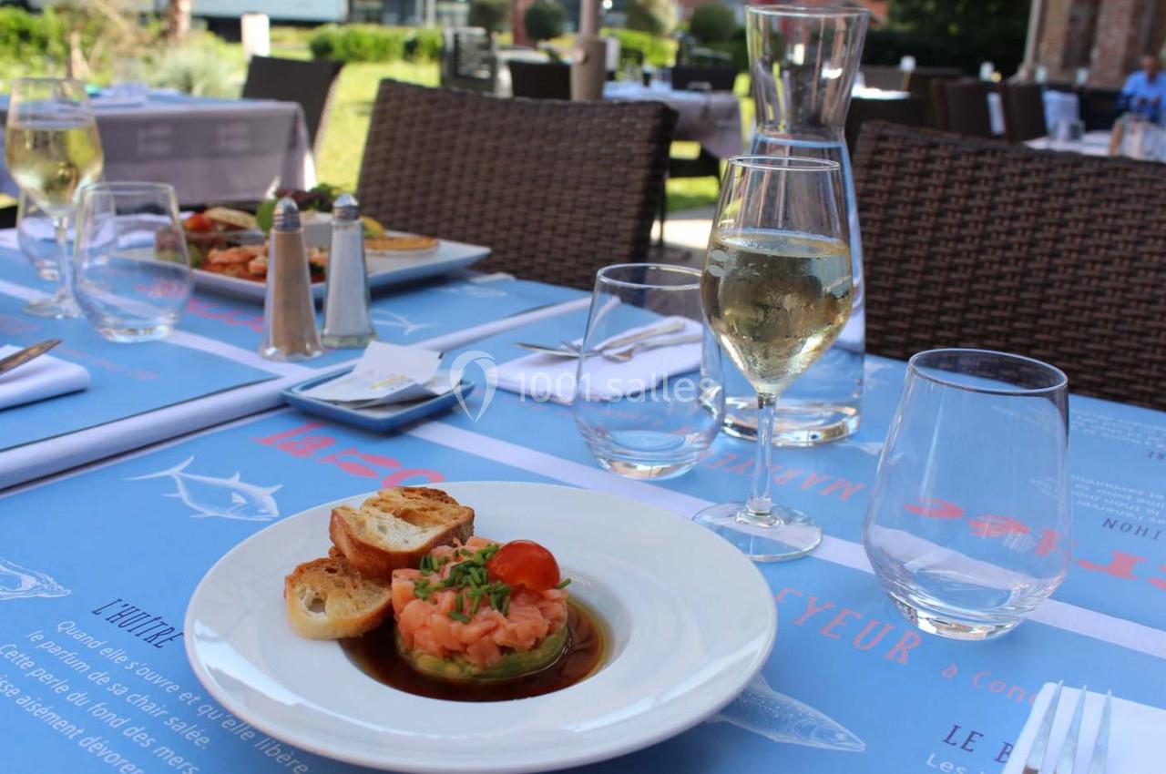 Assiette de tartare de saumon avec toasts, servie sur une table dressée en terrasse avec un verre de vin blanc.