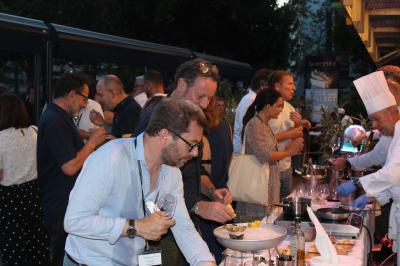 Des personnes se servent à un buffet en plein air, avec un chef en tenue blanche préparant des plats.