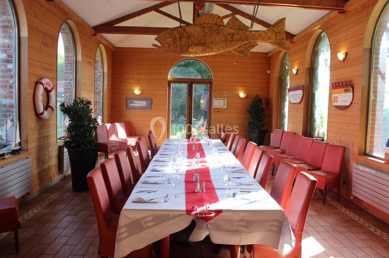 Salle de restaurant lumineuse avec une grande table dressée, entourée de chaises rouges et décorée d'éléments marins.