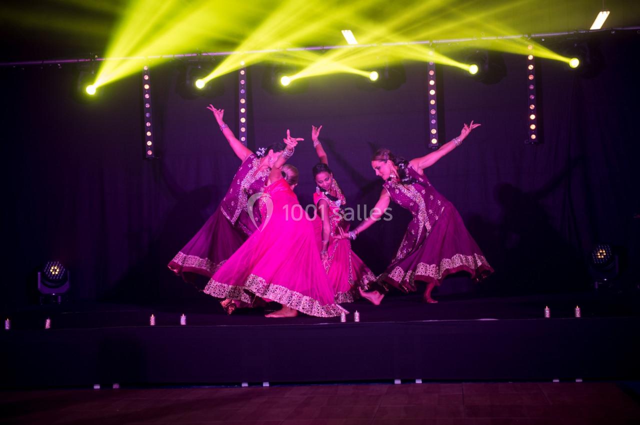 Danseuses en tenue traditionnelle rose et violette exécutant une chorégraphie sur une scène éclairée par des projecteurs…