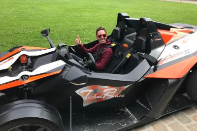 Un homme en costume noir et baskets blanches pointe du doigt sur une scène éclairée par des projecteurs.