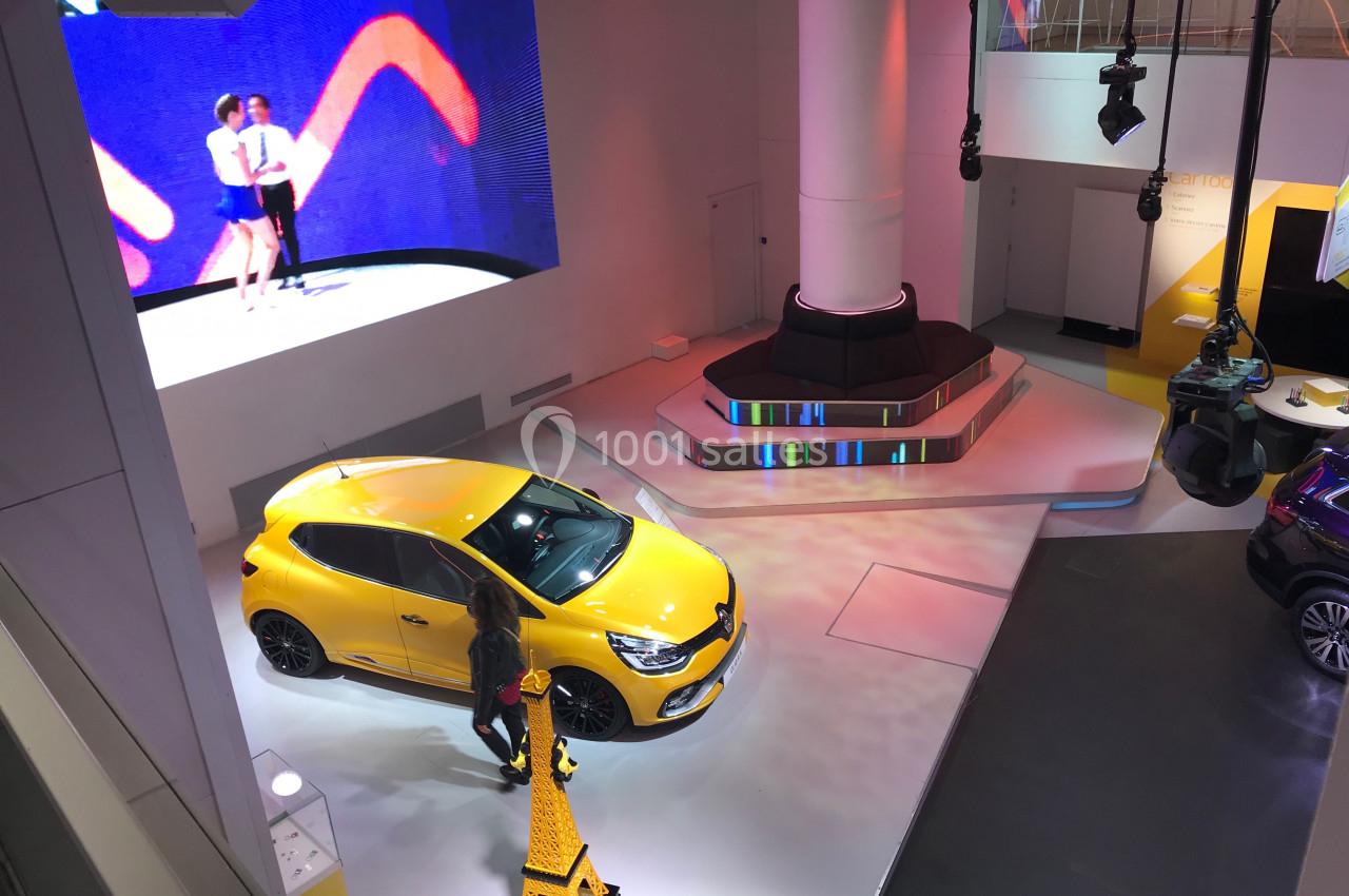 Vue d'une exposition automobile avec une voiture jaune, un écran affichant des danseurs et un éclairage coloré.