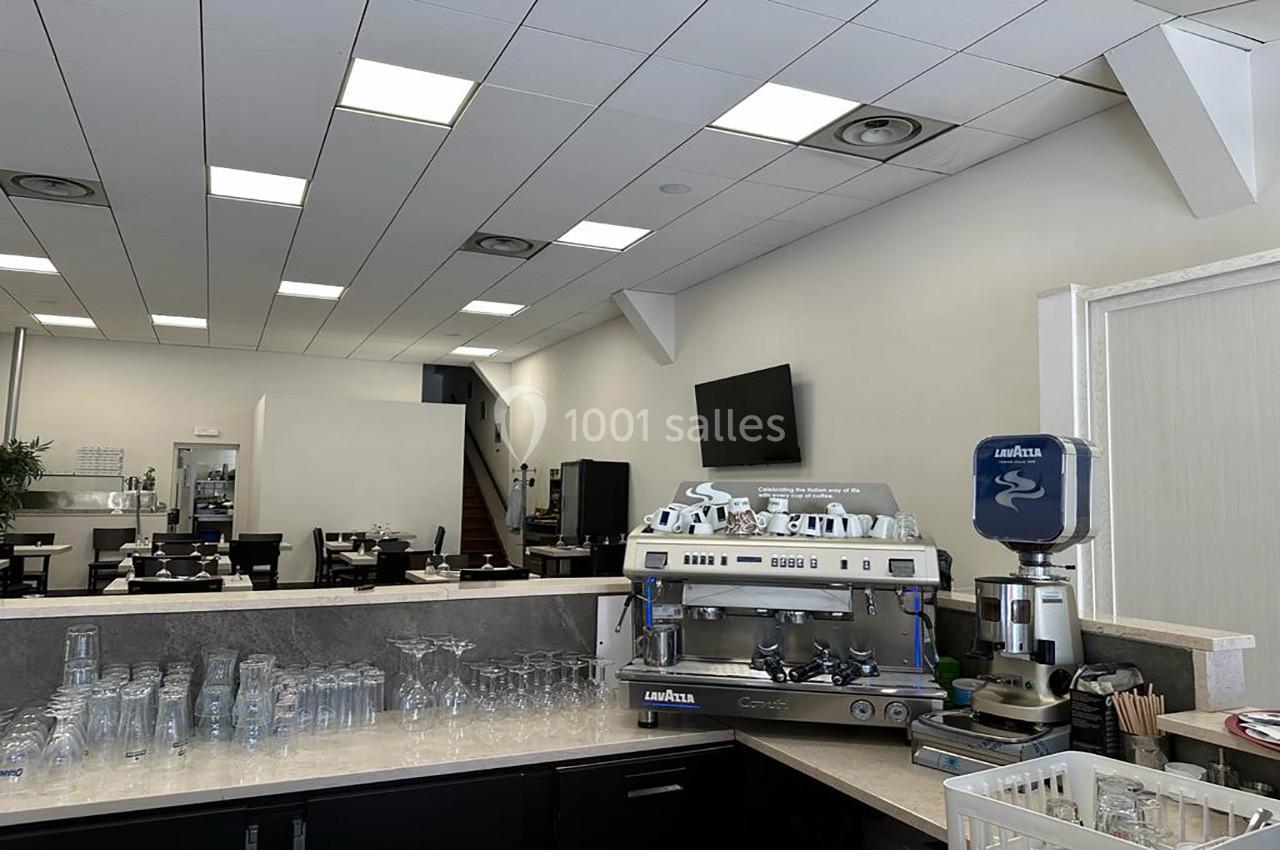 Salle de restaurant lumineuse avec un comptoir équipé d'une machine à café, un moulin à café et des verres alignés.