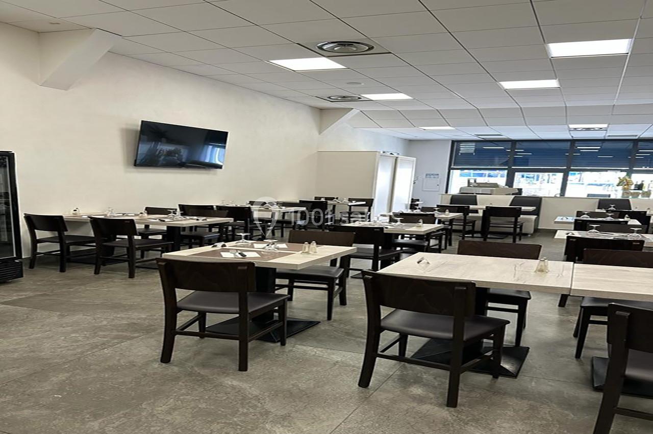Salle de restaurant moderne avec tables et chaises en bois sombre, éclairée par une grande fenêtre et des lumières au…