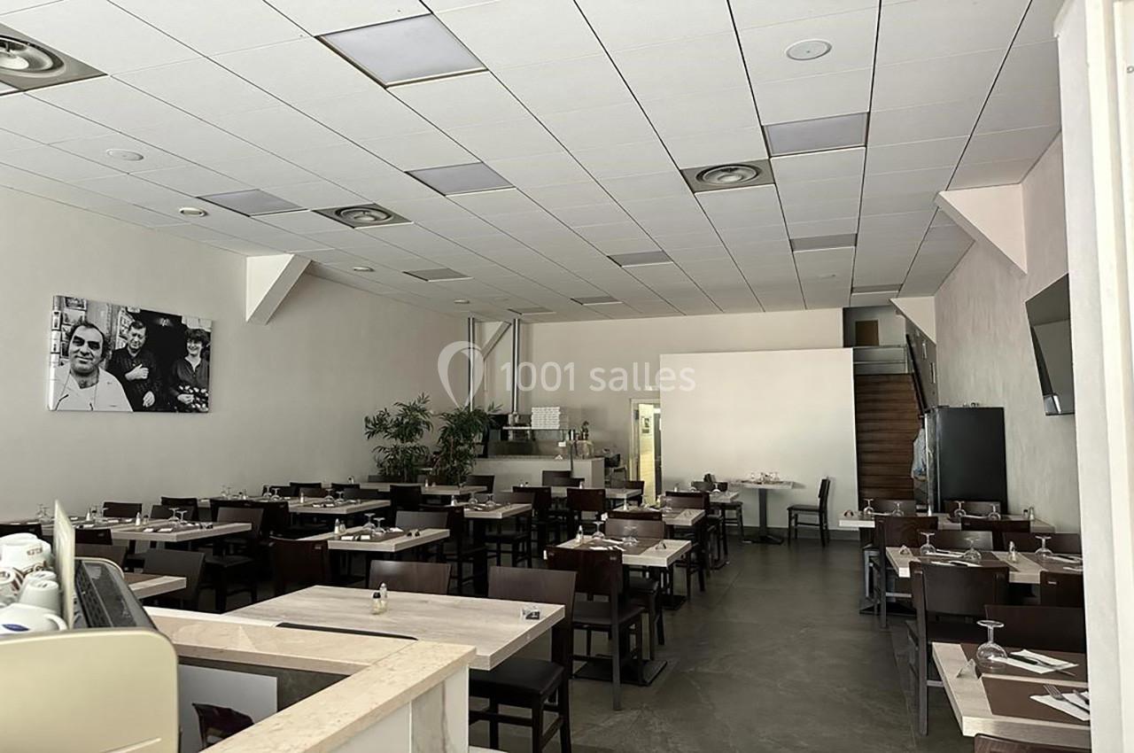 Salle de restaurant moderne avec tables dressées, chaises en bois foncé et décoration sobre.