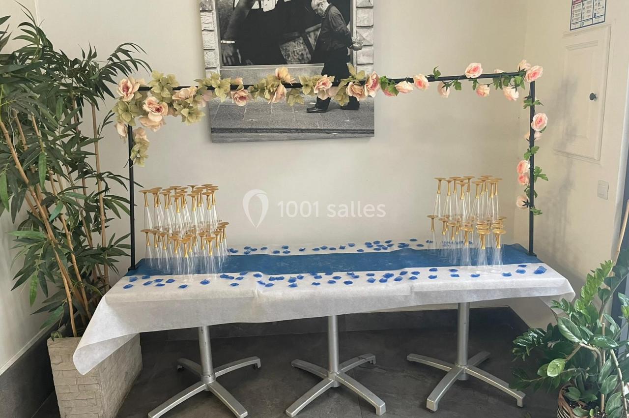 Table décorée avec des pétales bleus, des flûtes à champagne empilées et une arche ornée de fleurs roses.